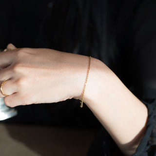 黒いトップスの袖口に、ゴールド色のあずきチェーン細ブレスレットを合わせた手元